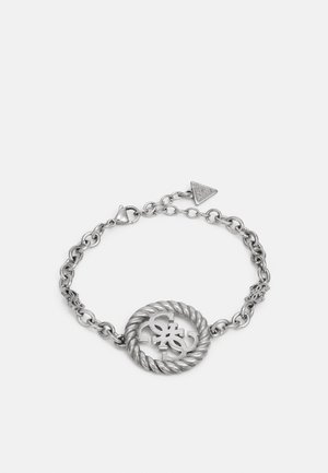 Bracelet chaîne en argent avec un centre circulaire torsadé présentant des lettres stylisées entrelacées et une petite étiquette de marque triangulaire.