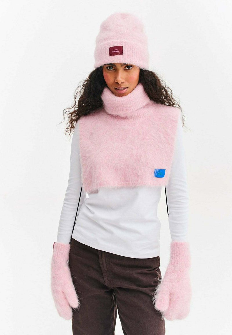 Różowa dziana czapka z metką, pasujący różowy puszysty szalik i rękawiczki. Strój składa się z białej bluzki i brązowych spodni. Miękkie tekstury w całej stylizacji.