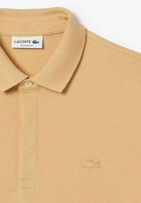 Beige Lacoste polo tröja i en texturerad tyg, med en knäppning med två knappar och broderad logotyp på vänster bröst. Regular fit-design.