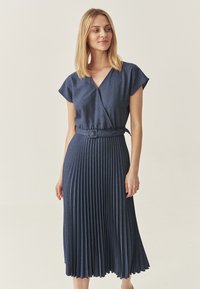 Wickelkleid aus dunklem Denim mit kurzen Ärmeln, plissiertem Rock und tailliertem Detail. Glatte Textur und knielanges Design.