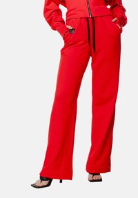 Czerwone dresy z luźnym krojem, z elastycznym paskiem i bocznymi kieszeniami. Wykonane z miękkiego materiału o gładkiej teksturze i szerokich nogawkach.