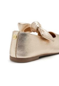 Ballet flat in oro metallico con un dettaglio a fiocco annodato sulla parte anteriore e un accento con logo circolare vicino al tallone. Materiale liscio e lucido.