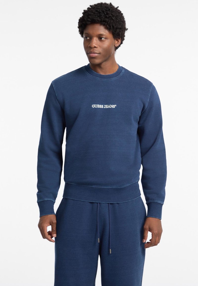 Marineblauwe sweatshirt van zachte stof, met een ronde hals en geribde manchetten. Inclusief het stiksel "GUESS JEANS" logo op de voorkant.