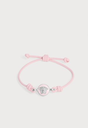 Justerbart pink snorearmbånd med rund sølv Medusa-hovedvedhæng og knudeender på hvid baggrund.