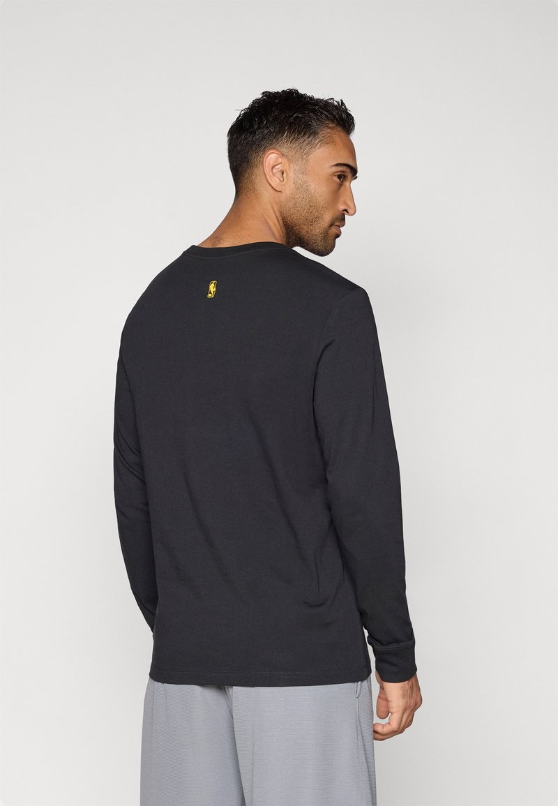 Camisa de manga larga negra de algodón, con cuello redondo y un pequeño logo amarillo en la parte superior de la espalda. Textura suave.