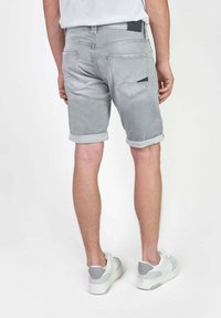 Grijze denimshorts met omgeslagen zomen, voorzien van achterzakken en een zwart label. Gepaard met witte sportschoenen met grijze accenten.