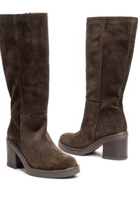 Botas de ante marrón hasta la rodilla con un tacón grueso. Presentan una punta redonda, cremallera lateral y detalle de costura en contraste en la suela.