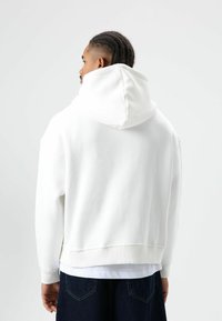 Witte hoodie met een losse pasvorm, zachte badstofstructuur, geribde manchetten en zoom. Zichtbare naden en een contrasterende voering van de capuchon.