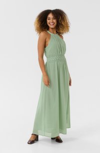 Maxi dress in light green, made of lightweight fabric. Features a pleated bodice, elastic waistband with lace detail, and sleeveless design.