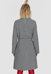 Zwart-wit houndstooth-gepatroneerde jas met lange mouwen, een ceintuur in de taille en een getailleerde snit. Gladde stof en een middellange uitvoering.