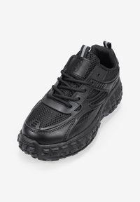 Black athletic shoe featuring a combination of textured mesh and smooth synthetic leather, designed with a rugged, traction-focused outsole.