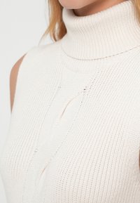 Πλεκτό αμάνικο τοπ με ριγέ υφή σε κρεμ απόχρωση και διακοσμητικό σχέδιο καλωδίου στο μπροστινό μέρος.