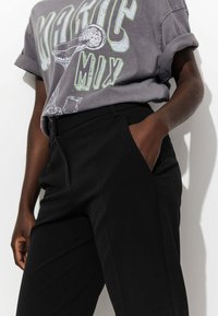 T-shirt graphique gris avec impression "Magic Mix", associé à un pantalon noir ajusté. Le tissu semble doux avec des manches retroussées et des poches latérales.