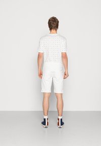 Camisa blanca de manga corta con un patrón repetido de veleros, combinada con pantalones cortos blancos y zapatillas altas con acentos en azul, rojo y blanco.