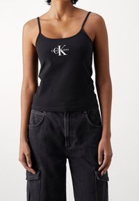 Czarny bawełniany top na ramiączkach, ozdobiony srebrnym logo Calvin Klein. W zestawie z ciemnoszarymi dżinsowymi spodniami cargo.