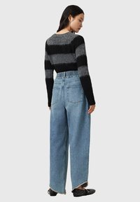 Maglione a righe nere e grigie, jeans in denim chiaro a vita alta con gambe ampie e scarpe nere con dettagli a borchie.