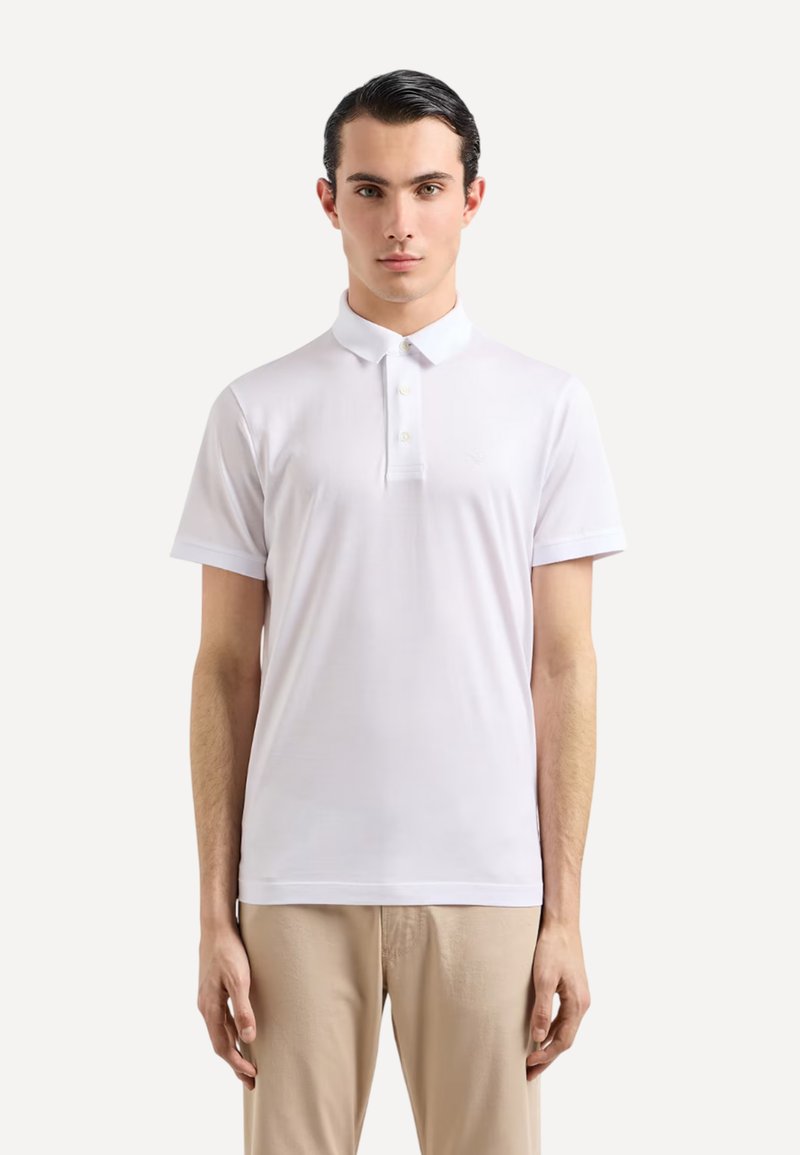 Polo shirt blanc à manches courtes avec un col classique, comportant trois boutons et un design légèrement ajusté. Tissu lisse et léger.