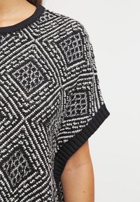 Haut en tricot noir et blanc avec un motif de losanges, à manches courtes et un col ras du cou côtelé. Tissu texturé avec des couleurs contrastées.