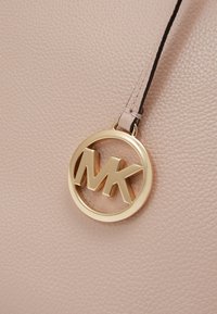 Lyserød pebret læder håndtaske med et fremtrædende guldfarvet cirkulært logo med "MK" initialer. Accentueret med en læderrem.