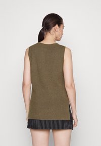 Top sem mangas verde-azeitona com textura canelada, apresentando uma bainha reta e fendas laterais, combinado com uma parte de baixo preta com riscas.