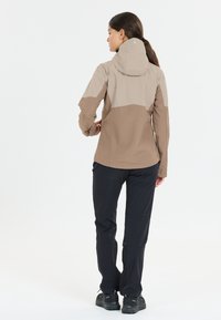 Lightweight, two-tone rain jacket with a beige upper and brown lower section. Features a hood and waterproof material, paired with black pants.