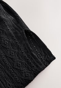 Black textured fabric with intricate diamond pattern and cutout detailing, featuring a side slit for added style and breathability.