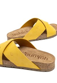 Sandalias cruzadas de ante amarillo con una plantilla de corcho y suela de goma. Presentan una plantilla texturizada con el nombre de la marca en relieve.