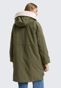 Parka jacket verde oliva con cappuccio foderato in pelliccia sintetica, vestibilità comoda, dettagli con zip sui lati e orlo posteriore leggermente più lungo.