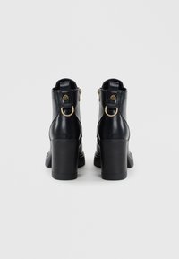 Stivali alla caviglia neri in pelle con tacco spesso, caratterizzati da un dettaglio in metallo dorato e due piccole asole sul retro per facilitare l'indossamento.