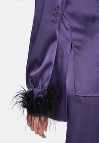 Purple satin blouse with long sleeves, featuring black feather trim on the cuffs and embellished details along the side seam.