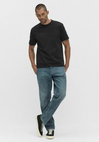 Svart bomulls-t-shirt med korta ärmar, kombinerad med ljusblå denimjeans och svarta sneakers med vit sula. Enkel, avslappnad outfit.