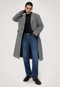 Szary wełniany płaszcz, dwurzędowy z klapami; zestawiony z ciemną koszulą, niebieskimi dżinsami i czarnymi skórzanymi butami.