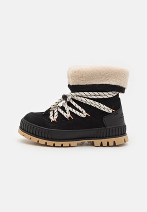 Svart semsket støvel med en tan gummisåle, kremfarget faux fur-kant og svarte og hvite mønstrede snøringer. Har solid konstruksjon og en teksturert overflate.