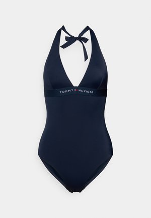 Tumši zils viengabala peldkostīms ar dziļu V-veida izgriezumu, kakla siksniņu un horizontālu joslu ar "TOMMY HILFIGER" logotipu. Gluda tekstūra un pieguloša forma.