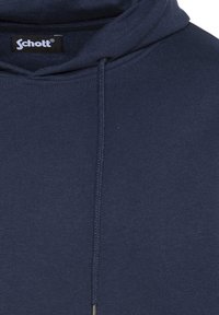 Felpa blu navy con cappuccio realizzata in tessuto morbido, dotata di cordoncino e una texture a costine attorno all'orlo e ai polsini. Etichetta Schott visibile.