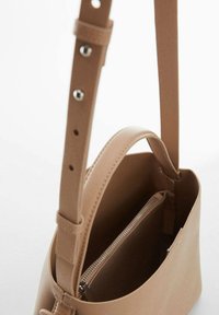 Sac à épaule en cuir beige clair avec une texture lisse, un design simple, une longue sangle réglable et une poche intérieure zippée.