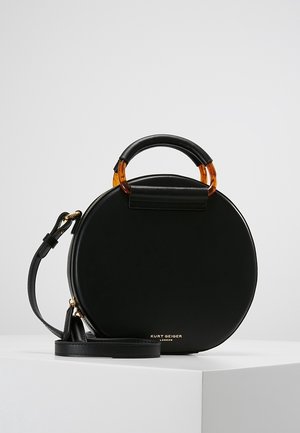 Ronde zwarte leren handtas met schildpad-handvat, verstelbare schouderriem en goudkleurig "Kurt Geiger London" logo aan de voorkant.