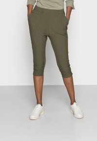 Olivgröna capribyxor med elastisk midja och sidofickor. Slät textur, avsmalnande nederkant, bärs med vita sneakers.