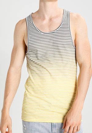 Homme portant un débardeur sans manches à rayures horizontales dégradant du gris au jaune, associé à un jean bleu clair déchiré.