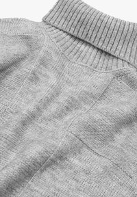 Nahaufnahme eines grauen, gestrickten Rollkragensweaters, der den gerippten Kragen und verschiedene Strickmuster am Körper und den Ärmeln zeigt.
