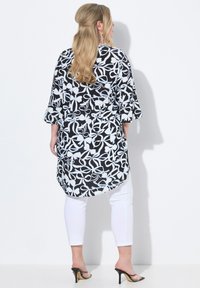 Blusa floreale in bianco e nero con maniche a tre quarti, caratterizzata da un orlo curvo e una vestibilità ampia, abbinata a pantaloni bianchi slim-fit e tacchi neri.