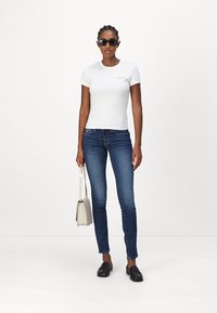 T-shirt bianco a maniche corte, jeans slim blu scuro, mocassini neri e una piccola borsa grigia.