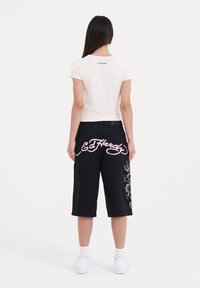 Camiseta de algodón rosa claro de manga corta, combinada con pantalones cortos de mezclilla negros que presentan texto bordado en rosa y patrones florales en la parte posterior.