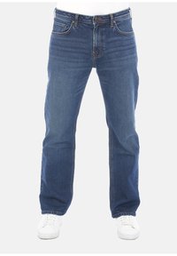 Jeans in denim blu con taglio dritto, dotati di cinque tasche, una cerniera frontale e leggeri segni di usura. Indossati con sneakers bianche.