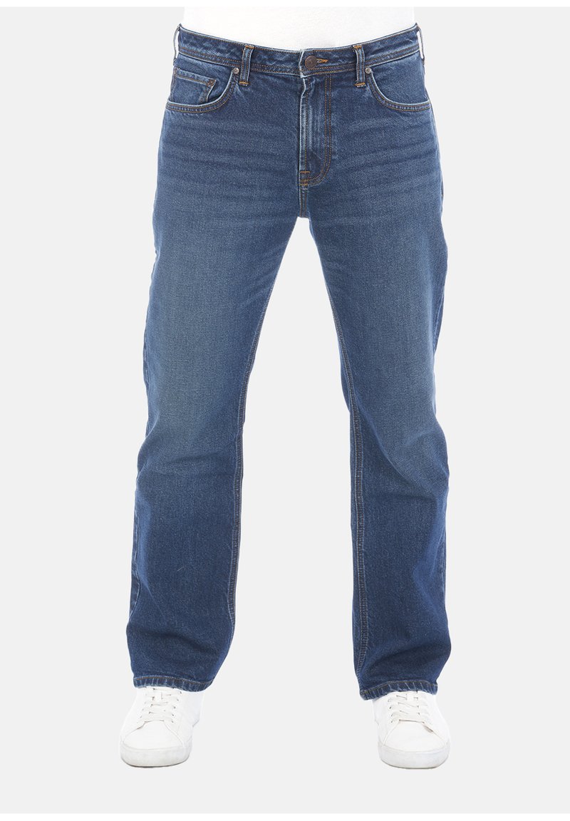 Jeans in denim blu con taglio dritto, dotati di cinque tasche, una cerniera frontale e leggeri segni di usura. Indossati con sneakers bianche.