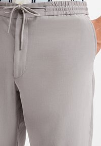 Helle graue Jogginghosen mit weicher Textur, elastischem Bund und verstellbarem Kordelzug. Mit Seitentaschen und taillierter Passform.