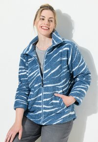 Fleecowa kurtka w niebiesko-białe wzory, z wysokim kołnierzem, pełnym zamkiem i przednimi kieszeniami. Tekstura jest miękka i puszysta.