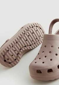 Ljusrosa träskor i texturerad gummi, med ventilationshål, bakrem och en räfflad sula för bra grepp.