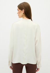 Witte blouse met lange mouwen, gemaakt van een soepele stof, met een ronde zoom en knoopsluiting bij de manchetten, en een eenvoudig achternaadontwerp.