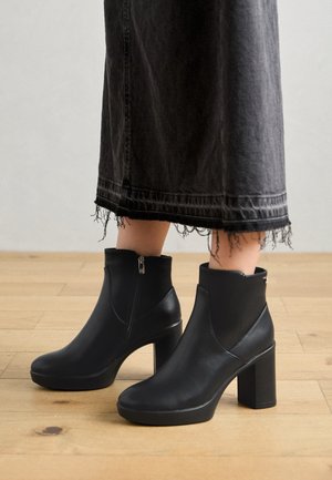 Bottes basses en cuir noir avec un bout arrondi, un talon bloc haut et une fermeture éclair latérale ; associées à une jupe en denim noir à ourlet effiloché.